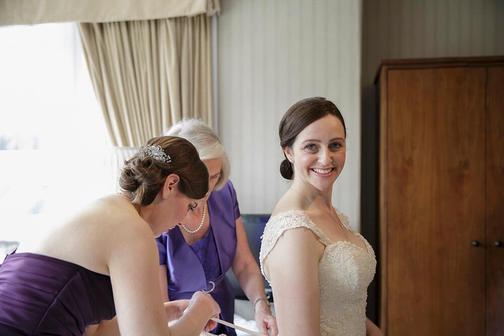 Bridal Prep - ©LouiseMallanPhotography - Bride getting helped into her dress by mum and bridesmaid